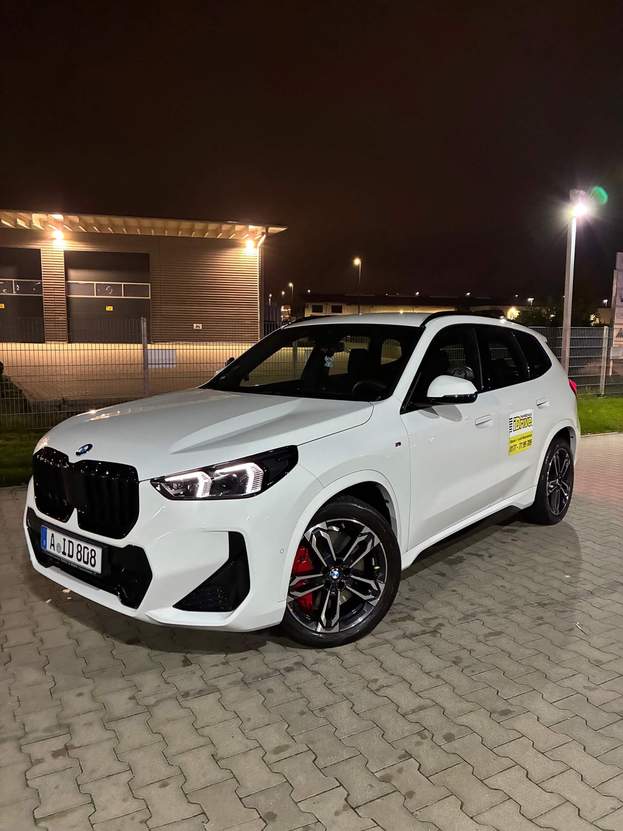 Weißes iDrive Fahrschulfahrzeug bei Nacht